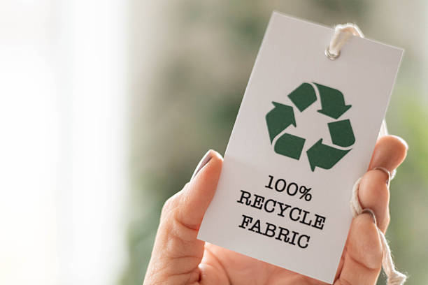 istock Hand holding recycled fabric tag on sustainable clothing stack, eco textile concept 2237290409