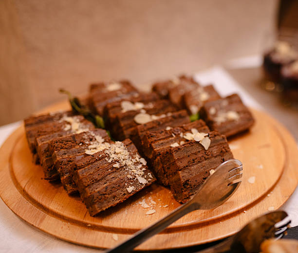 A warm dessert table featuring rich chocolate brownies sliced on a wooden board, with small layered dessert cups visible in the background. Perfect for catering, gatherings, and holiday spreads