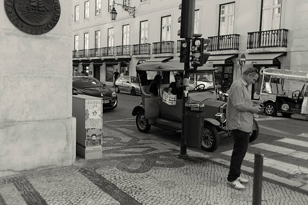 Lisbon, Portugal - November 2, 2024: A tuk-tuk driver extends a menu card while sitting inside his tuk-tuk, waiting for clients in Lisbon downtown.