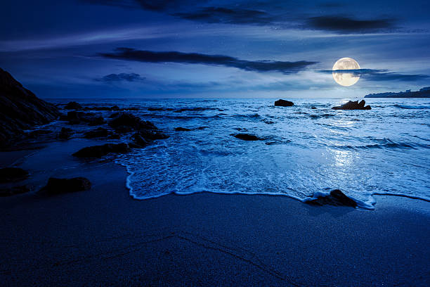 istock calm sea landscape with wave rolling on sandy beach with boulders at night 2237301391