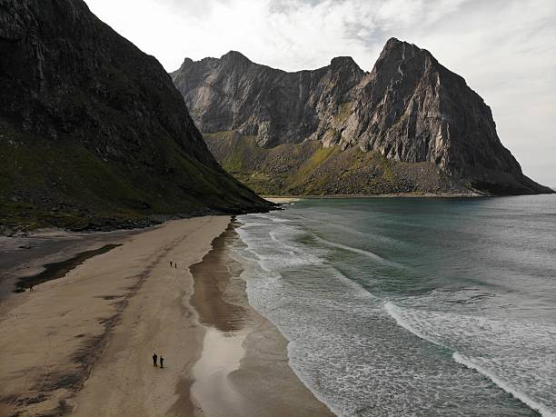 Drone view of a wide sandy beach surrounded by dramatic mountain cliffs and turquoise water in Norway.