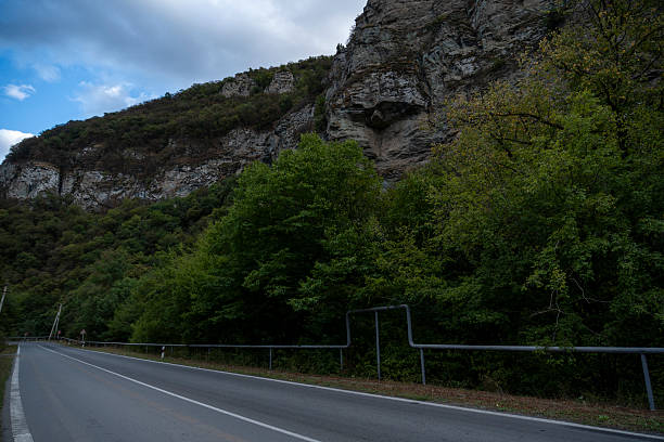 istock Empty winding mountain road leading through lush forest to rocky mountains 2237312710