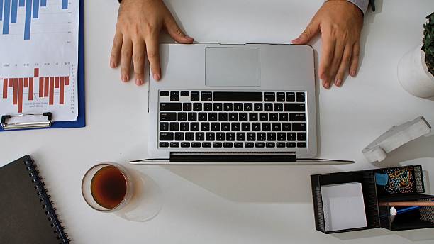 Top view of a workspace featuring a laptop, charts, a desk organizer, and a cup of coffee, showcasing a professional setting.