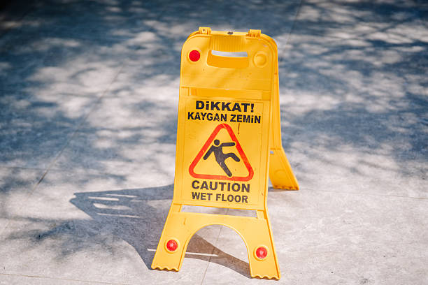 Kemer, Tureky - september 18, 2025 - Yellow plastic caution sign with warning text in Turkish and English, indicating a wet floor. Placed on a sunlit tiled surface casting shadows.