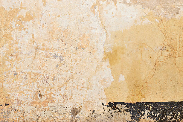 Old Weathered Wall Texture With Peeling Plaster And A Dark Baseboard Along The Bottom