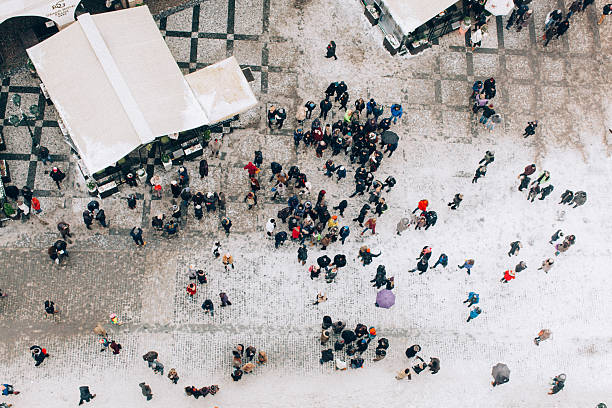 An aerial shot capturing a bustling crowd gathered in a snowy public square, surrounded by festive stalls and winter scenery.