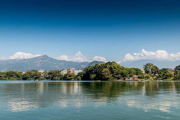 This stunning landscape showcases the tranquil waters of Fewa Lake in Pokhara with the iconic Machhapuchhre (Fishtail Mountain) and Annapurna range in the background. The clear reflection of mountains and greenery creates a perfect harmony between city and nature. It represents Pokhara’s charm as a gateway to the Himalayas, blending serene waters, vibrant culture, and majestic snow-capped peaks under a bright blue sky.