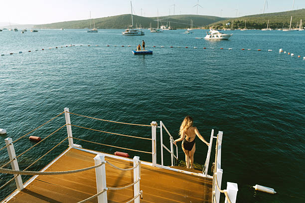 A photo of a brunette woman in her 20s climbing pier steps at sunset, with the sea in the background, capturing the warm hues and serene atmosphere