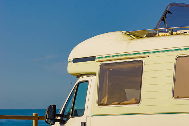 Rv camper vehicle with open sunroof, raisable panel window on roof top against blue sky. Traveling by motor home.
