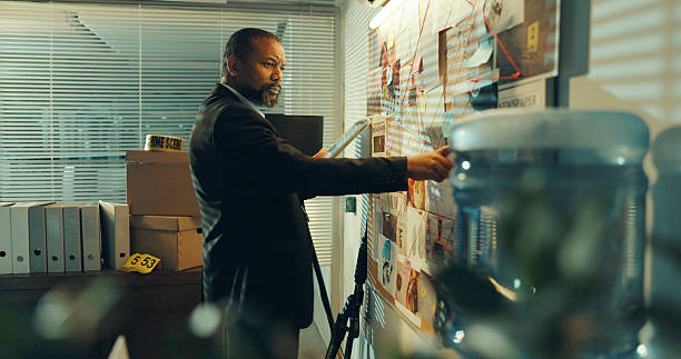 istock Man, detective and tablet at board for crime, pointing at evidence or documents with link for criminal case. Mature African policeman, tech for investigation or problem solving with analysis at night 2237334450