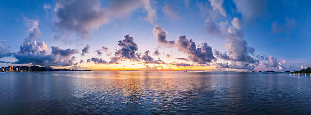 Dramatic panoramic seascape with a beautiful golden sunset on the horizon and clouds reflected in the calm ocean water.