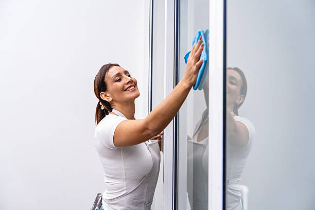 A woman manually washes the window of the house with a rag with a spray cleaner and a mop outside. Safety at height, restoring order and cleanliness in the spring, cleaning service