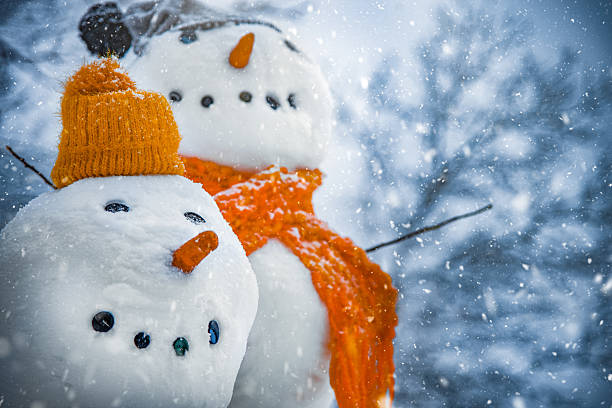 Two Snowmen With Orange Hat And Scarf In Winter Snowfall
