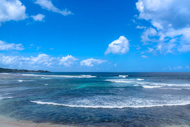 Sunlit Bali coast with clear blue water and gentle waves rolling onto a sandy shore under a bright sky. A peaceful tropical seascape perfect for travel, relaxation, and nature themes.