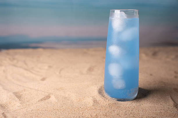 istock tall glass of refreshing blue beverage with ice cubes on sandy beach setting, creating a calm and inviting atmosphere with a backdrop of soft blue ocean waves and serene sky, beachside, glassware 2237352110