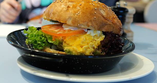 Burger features scrambled egg on table against visitor eating in restaurant