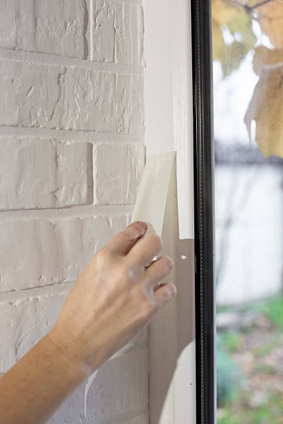 istock A hand removes masking tape from a white window frame next to a painted brick wall 2237355625