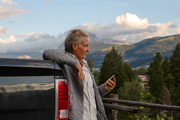 istock Mature man relaxes against vehicle using mobile phone 2237364527