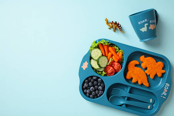 istock Dinosaur-themed tray with nuggets, veggies, and blueberries. Includes matching cup and toy for a fun, nutritious kids meal setup. 2237376575