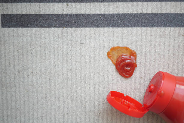 A bright red ketchup stain marks a striped rug, cap open nearby.