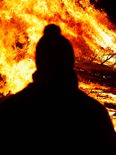 istock Person is standing in front of a fire, with their head turned away 2237389889
