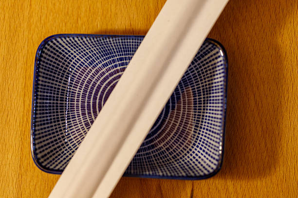 A beautifully arranged flat lay composition of traditional Thai blue and white ceramic plates and bowls, accompanied by wooden chopsticks, placed on a soft neutral fabric background. The intricate patterns on the dishware reflect Thai craftsmanship and cultural aesthetics. The minimalist yet elegant dining setup creates a warm and inviting atmosphere, making this image ideal for restaurant branding, food styling, Asian cuisine promotions, and interior design concepts.