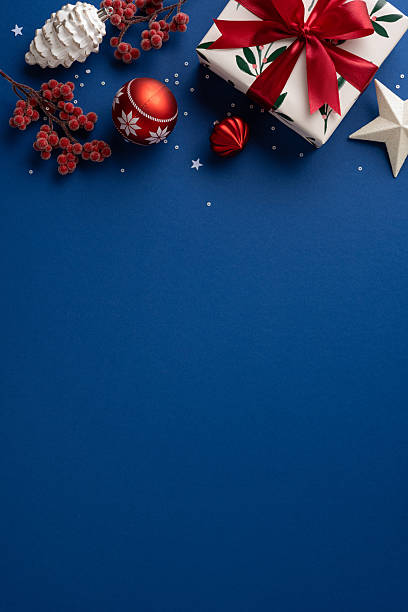 istock A vertical gift box with red ribbon, ornaments, and berries sits on a deep blue backdrop, evoking Christmas and New Year celebration and warm seasonal greetings 2237400396