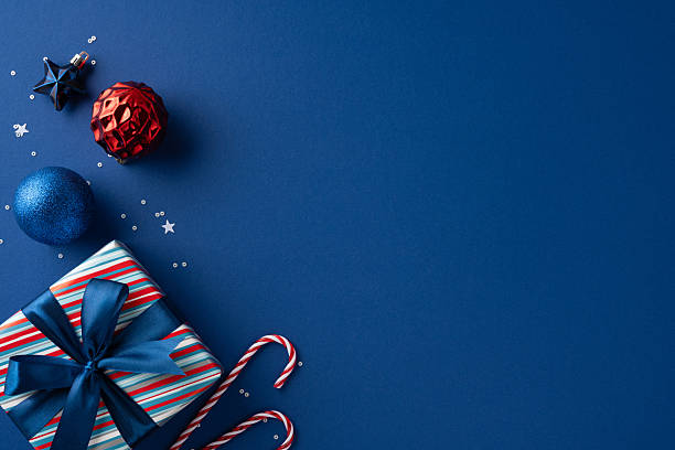 istock A festive scene featuring a striped gift box with blue ribbon, blue and red ornaments, and candy canes scattered on a dark blue backdrop to evoke holiday cheer 2237400439