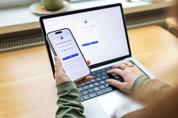 istock Close-up of woman entering two-factor authentication from phone into  computer in office 2237401275