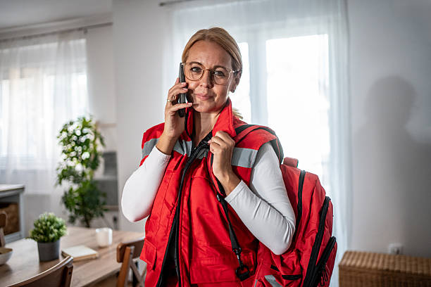 Mid-40s female healthcare worker in red uniform arrives for a home visit, speaking on mobile phone and carrying a first aid kit, confident and ready to provide emergency care