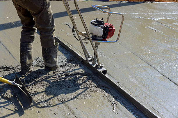 Construction worker uses power trowel to create smooth concrete surface on works day.