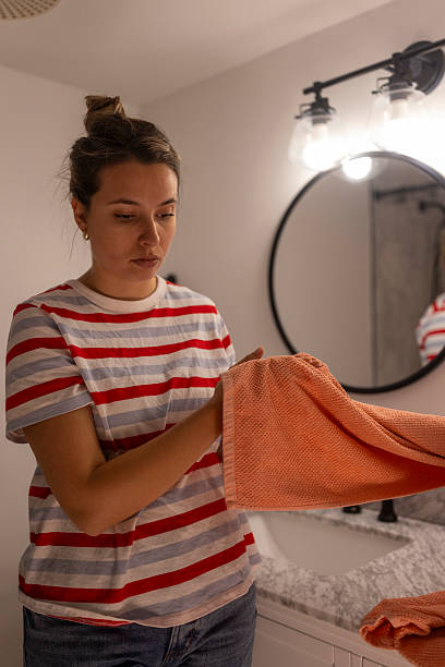 istock Young Woman Folding Bright Orange Towel in Bathroom 2237429237