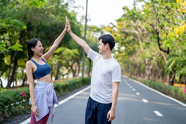 istock Asian young couple making high five while exercise outdoors in garden. Attractive man and woman resting and taking a break while practice workout for health care in park during sunrise after wake up. 2237434200