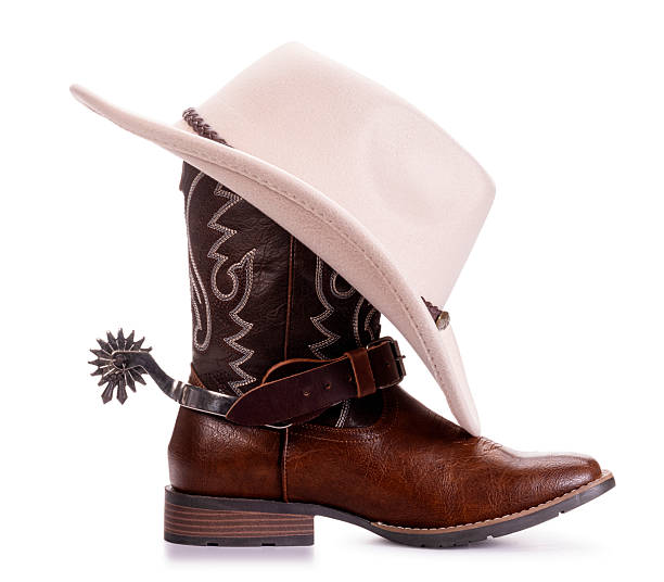 Western cowboy boot with decorative stitching and metal spur, paired with a classic beige cowboy hat angled stylishly on top, isolated on a clean white background. Rustic brown leather boot with strap and pointed toe, authentic western rodeo style, perfect for country themed designs, ranch culture concepts, Texas or Southwestern fashion, cowboy gear, horseback riding accessories, Wild West iconography, and American western heritage visuals.