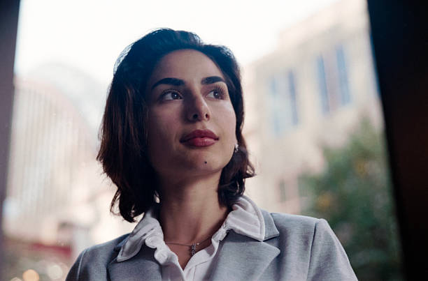 Thoughtful young adult business woman wearing a blazer and white shirt, looking up with hope, contemplating the future and new opportunities in an urban environment with film grain