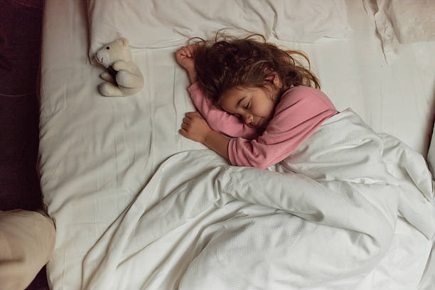 istock Little girl sleeping peacefully in bed with teddy bear 2237451323