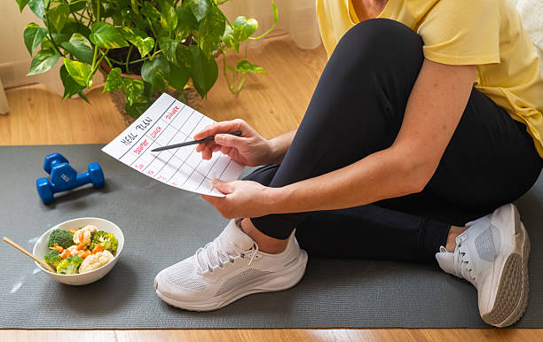 istock After a workout, a woman plans her nutrition in a notepad while sitting on a mat with a dumbbell and a salad, representing mindful eating and fitness lifestyle. 2237451901