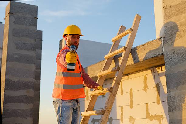 istock Construction worker using cordless drill on wooden ladder at building site 2237455221