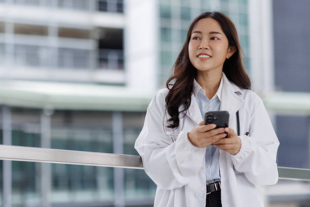 istock Asian doctor smiling and typing message on smartphone 2237458520