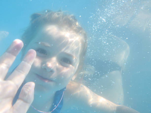 Young girl making eye contact while waving underwater in a swimming pool on a sunny day