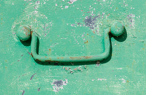 A green handle with a rusted metal ball on each end. The handle is attached to a green box