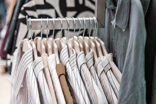 istock A rack displaying neatly arranged striped and solid shirts in a retail store. The shirts are hanging on wooden hangers, showcasing various colors and patterns. 2237461260