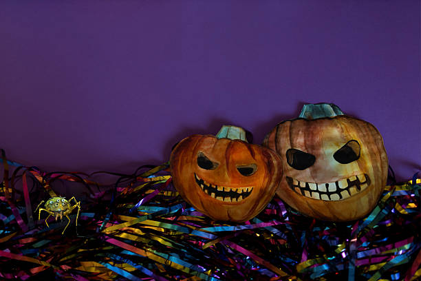 A hand-painted jack-o'-lantern pumpkin with a friendly smile sits on a bed of shimmering, colorful metallic streamers. The contrast between the dark setting and the vibrant elements highlights the whimsical yet traditional Halloween feel. This simple yet eye-catching composition is perfect for Halloween-themed promotions, party invitations, festive backgrounds, or seasonal designs that blend spooky charm with playful energy.