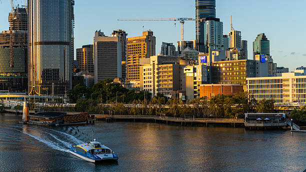 Brisbane city skyline with riverside buildings and a CityCat ferry on the Brisbane River.