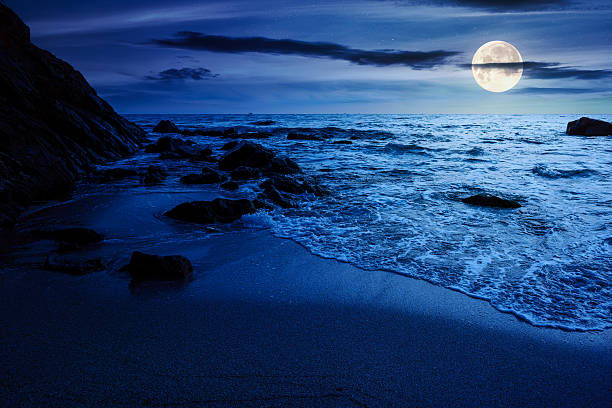 istock calm sea landscape with wave rolling on sandy beach with boulders at night 2237464341