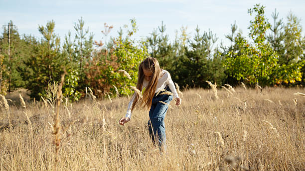 Child girl walking alone in field at sunset
