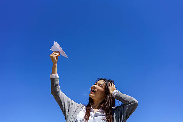 istock Woman holding paper airplane under clear blue sky 2237470122