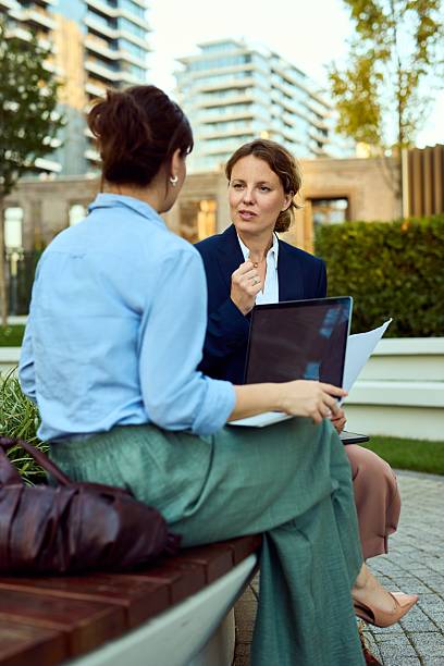 istock Professional Women Discuss Strategy Outdoors On A Bench With Laptop And Documents 2237470568
