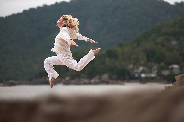 Tanned blonde female jumping into the air at the beach.