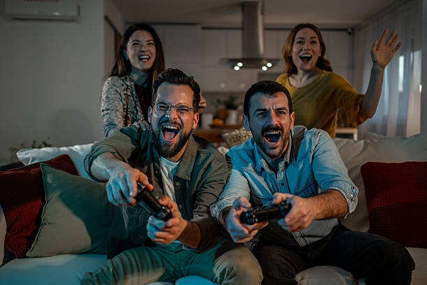 Cheering friends spending time together at home, playing video games with controllers on the couch, experiencing pure excitement and joy during their leisure activity
